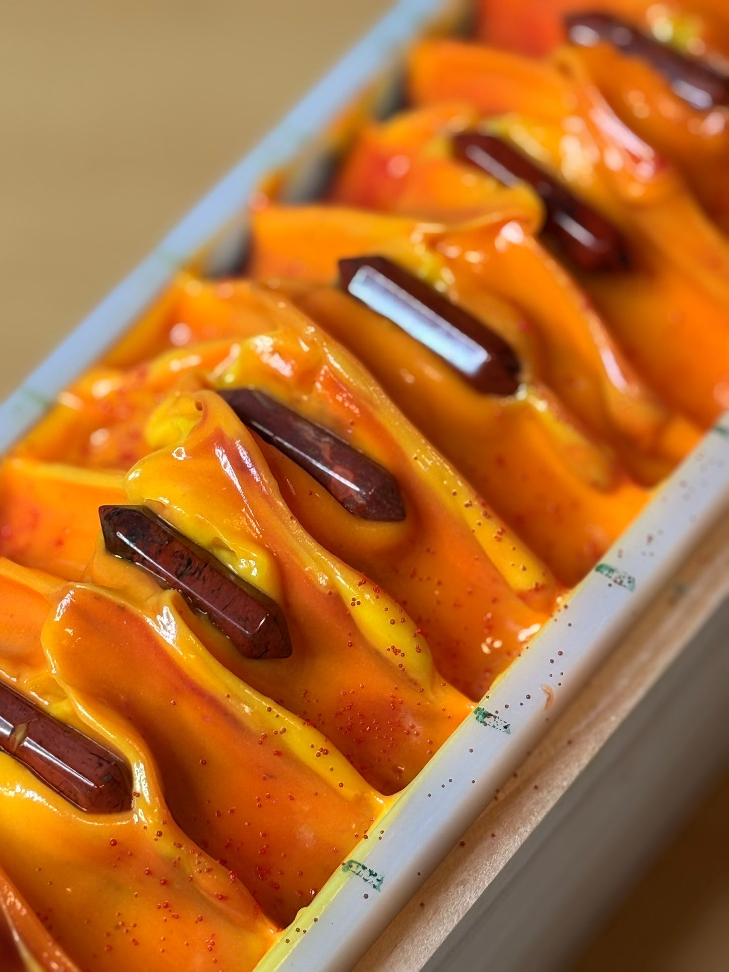 The top of an uncut soap loaf that is predominantly orange and displays red jasper stones on top.