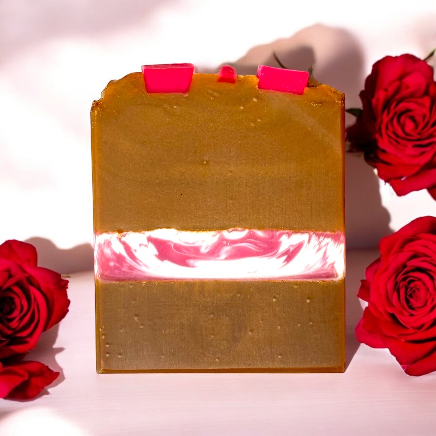 A bar of soap with a strawberries and cream fragrance, topped with pink hearts on a caramel colored swirl, displayed alongside red roses.