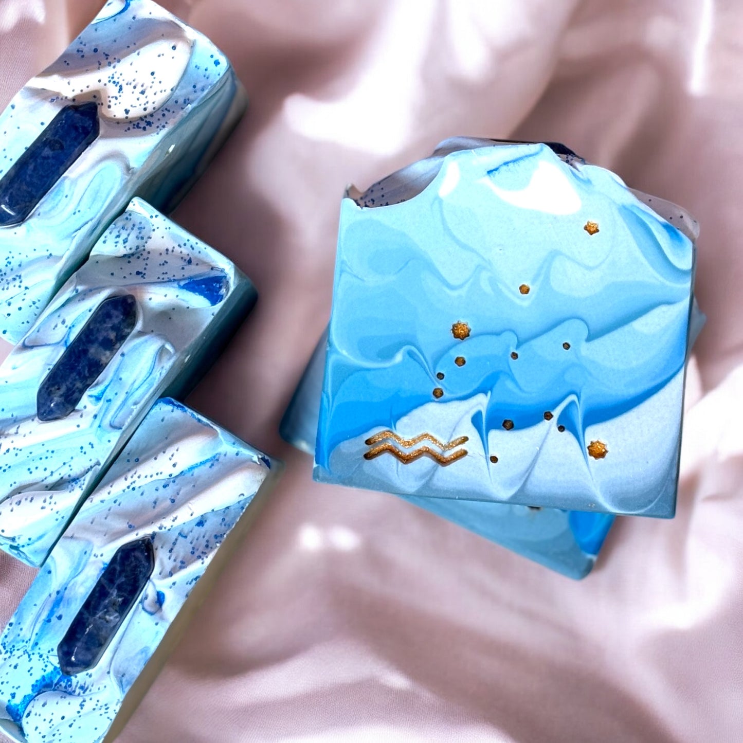 A bar of soap with a liquid blue design featuring gold stars and the Aquarius symbol stamped on the front, with a blue crystal on top.