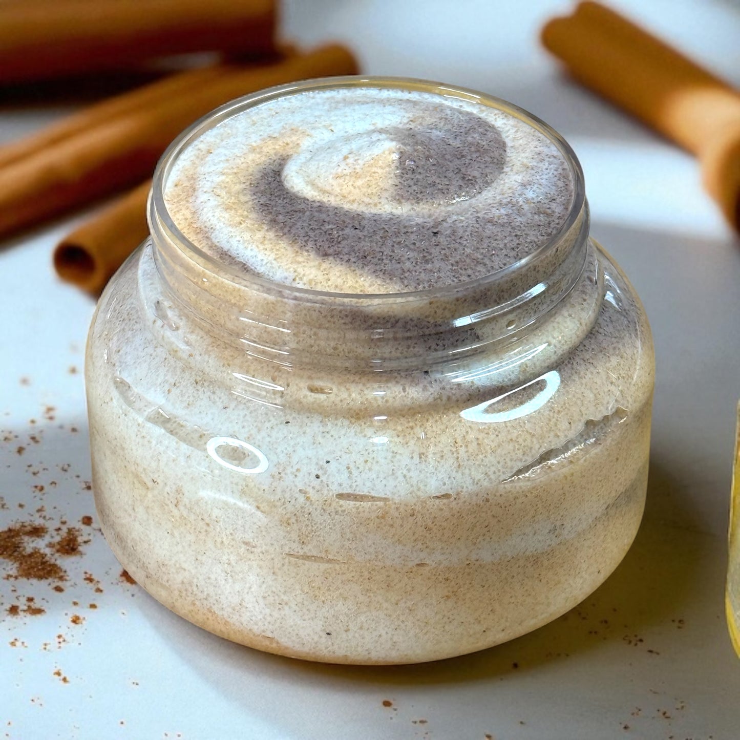Jar of cinnamon sugar scented sugar scrub in shades of brown and gold with cinnamon sticks in the background