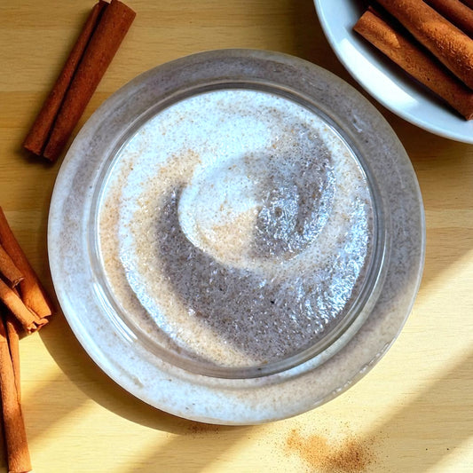 Jar of cinnamon sugar scented sugar scrub in shades of brown and gold with cinnamon sticks in the background