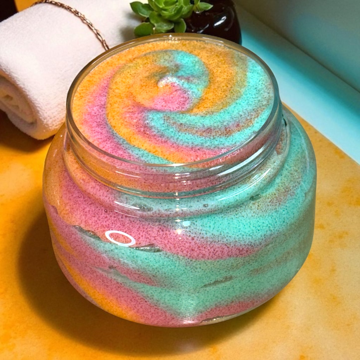 Colorful sugar scrub in a clear plastic jar on a wooden surface.