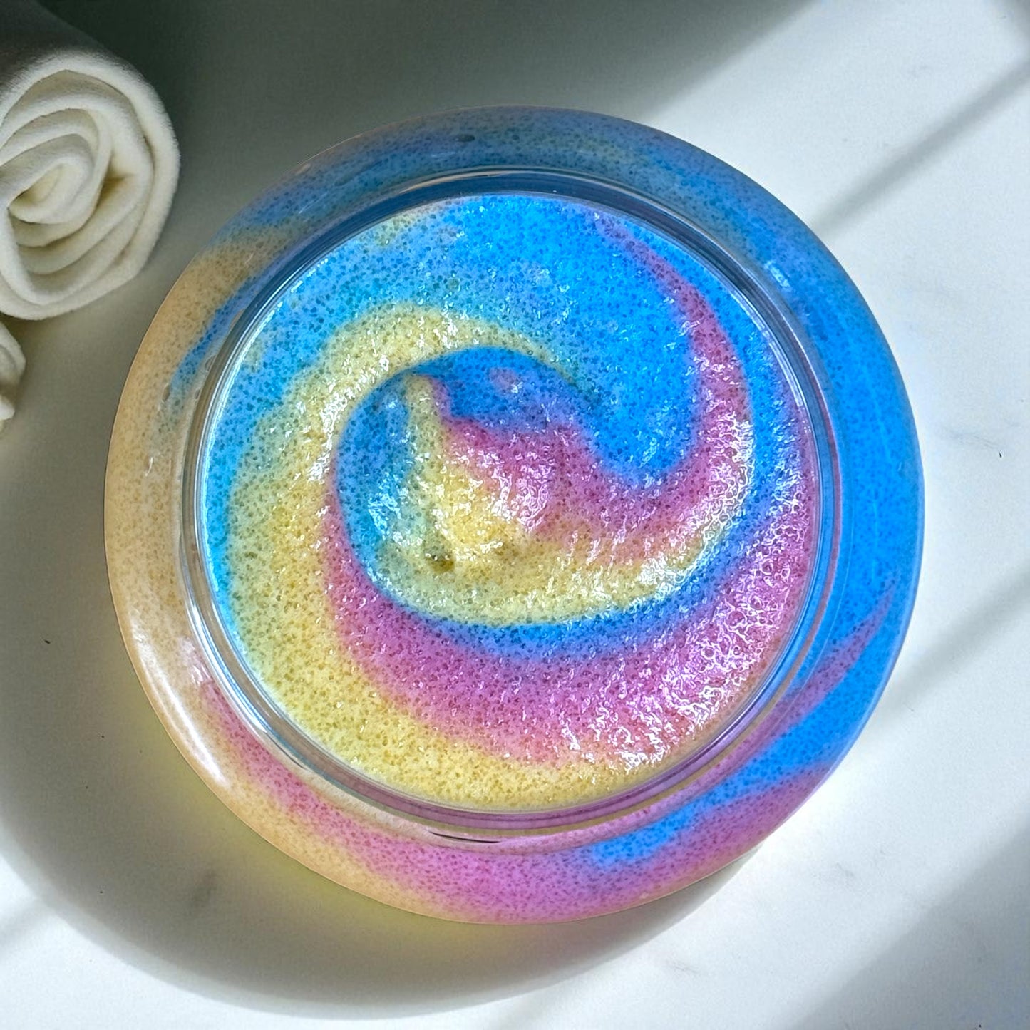 Colorful swirled sugar scrub in a clear plastic container on a white surface