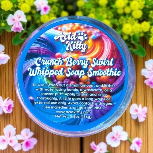 Container of Acid Kitty Crunch Berry Swirl Whipped Soap Smoothie with colorful label on a wooden surface with flowers.