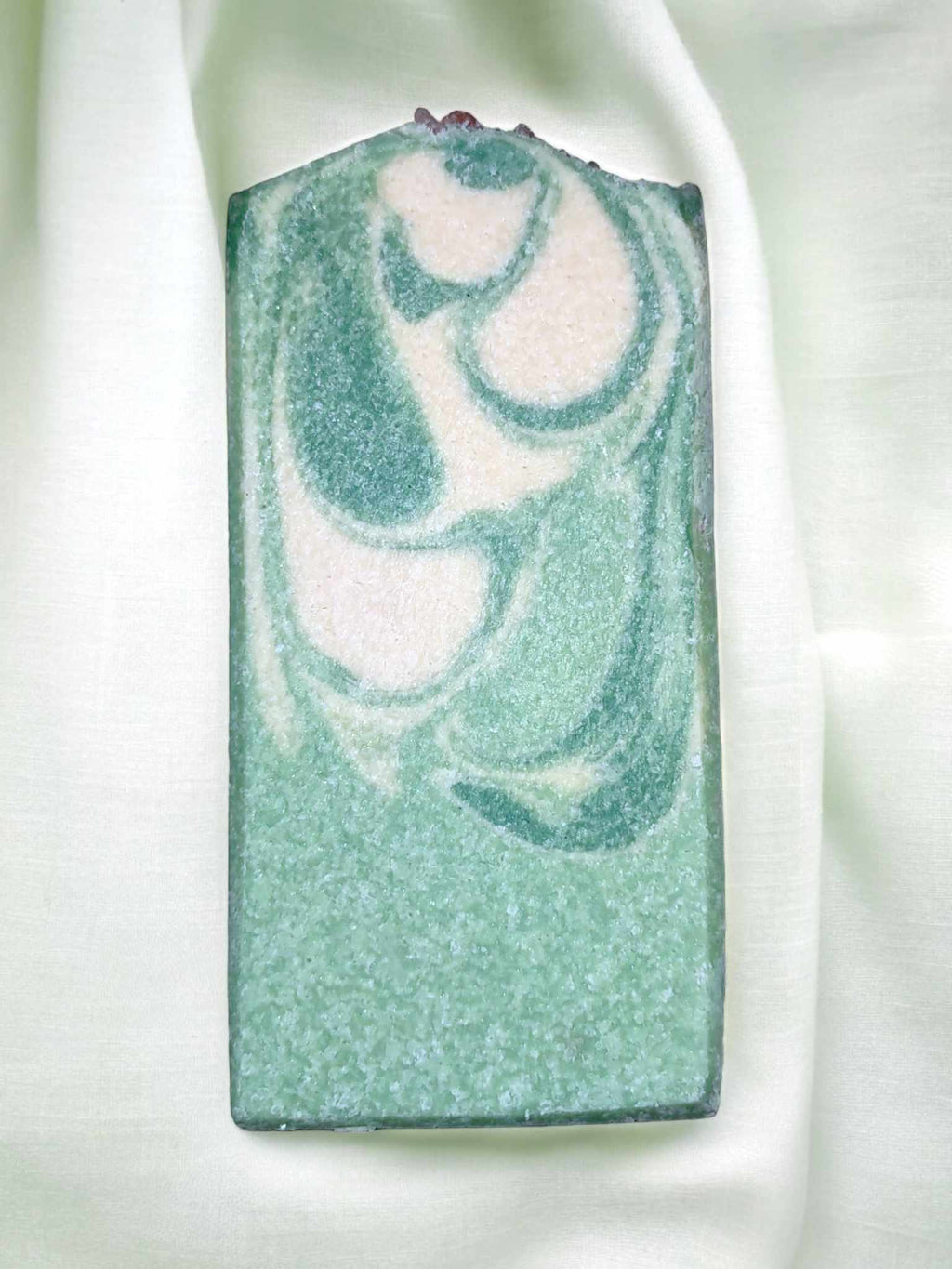 A bar of handmade salt soap with a green and white swirled pattern on a white background. 