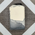A gray and white bar of soap with an obsidian stone embedded on top. 