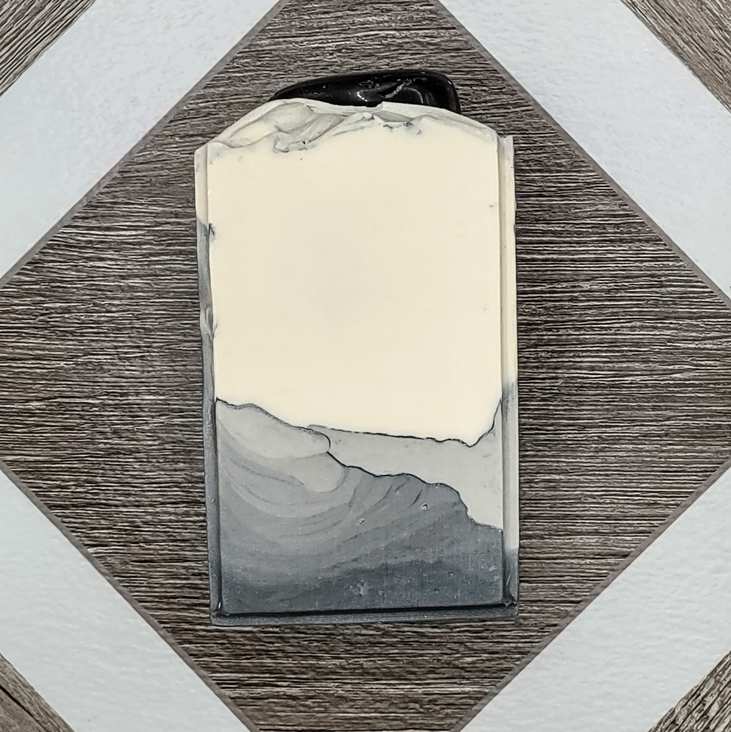 A gray and white bar of soap with an obsidian stone embedded on top. 