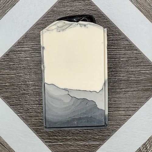 A gray and white bar of soap with an obsidian stone embedded on top. 