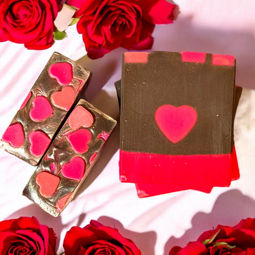 A bar of soap with a chocolate brown color and a red heart design on top and in the middle, presented alongside red roses.