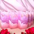 A row of rectangular bars of soap with an ombre pink to purple color gradient, displayed with a pink draped background and red roses in the foreground.