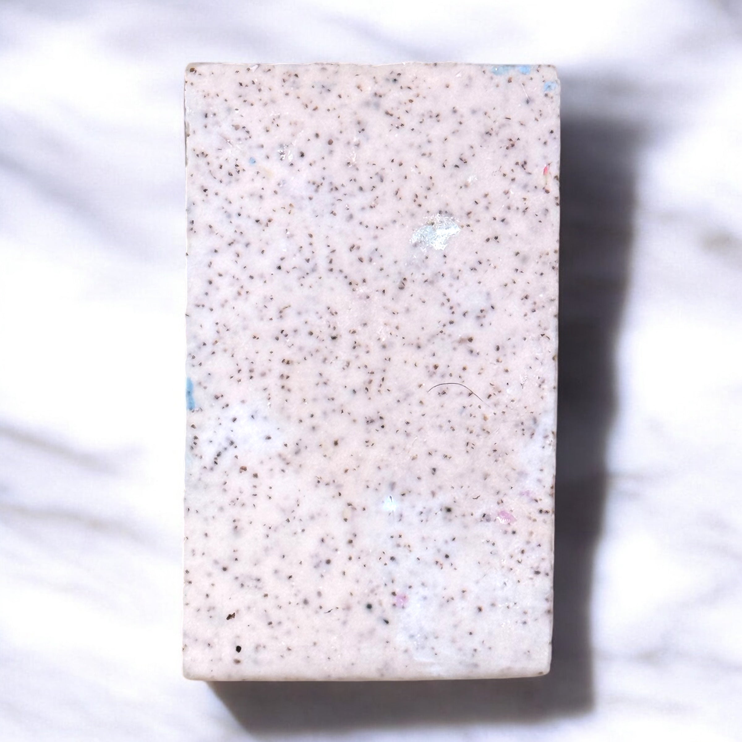 One bar of artisan soap displaying the back, which is white with flecks of walnut shell powder, displayed on a marble surface.
