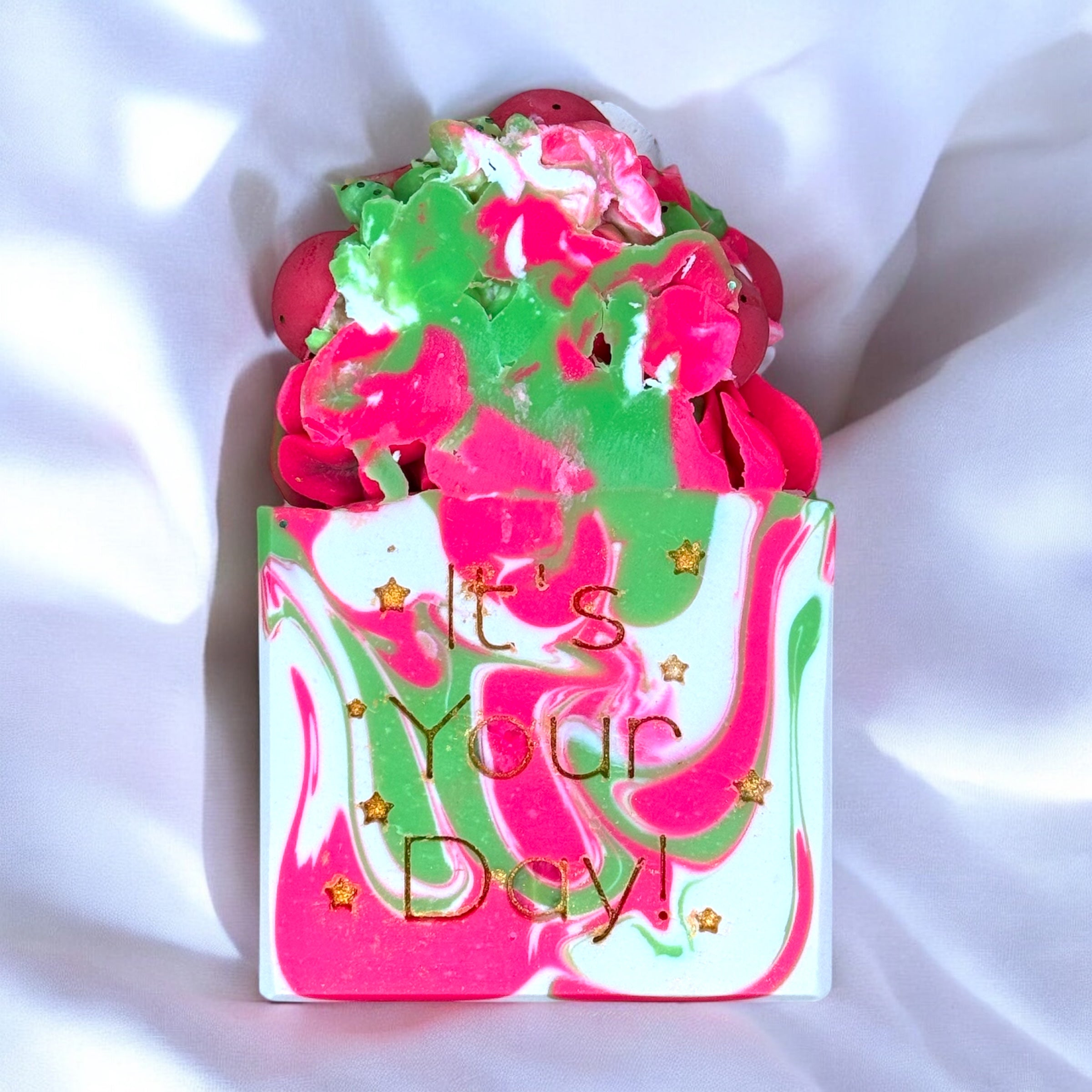 A bar of strawberry kiwi scented soap with a colorful design featuring predominantly pink and green hues, and text that reads 'It's Your Day!'.