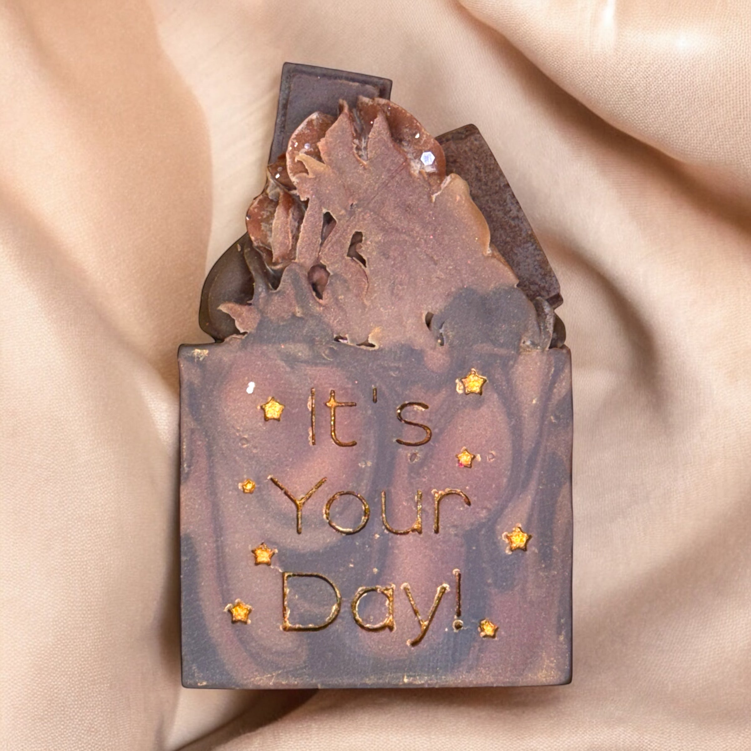 A bar of soap with a fudge brownie design, topped with mini chocolate bars, and the text 'It's Your Day!' stamped on the surface.