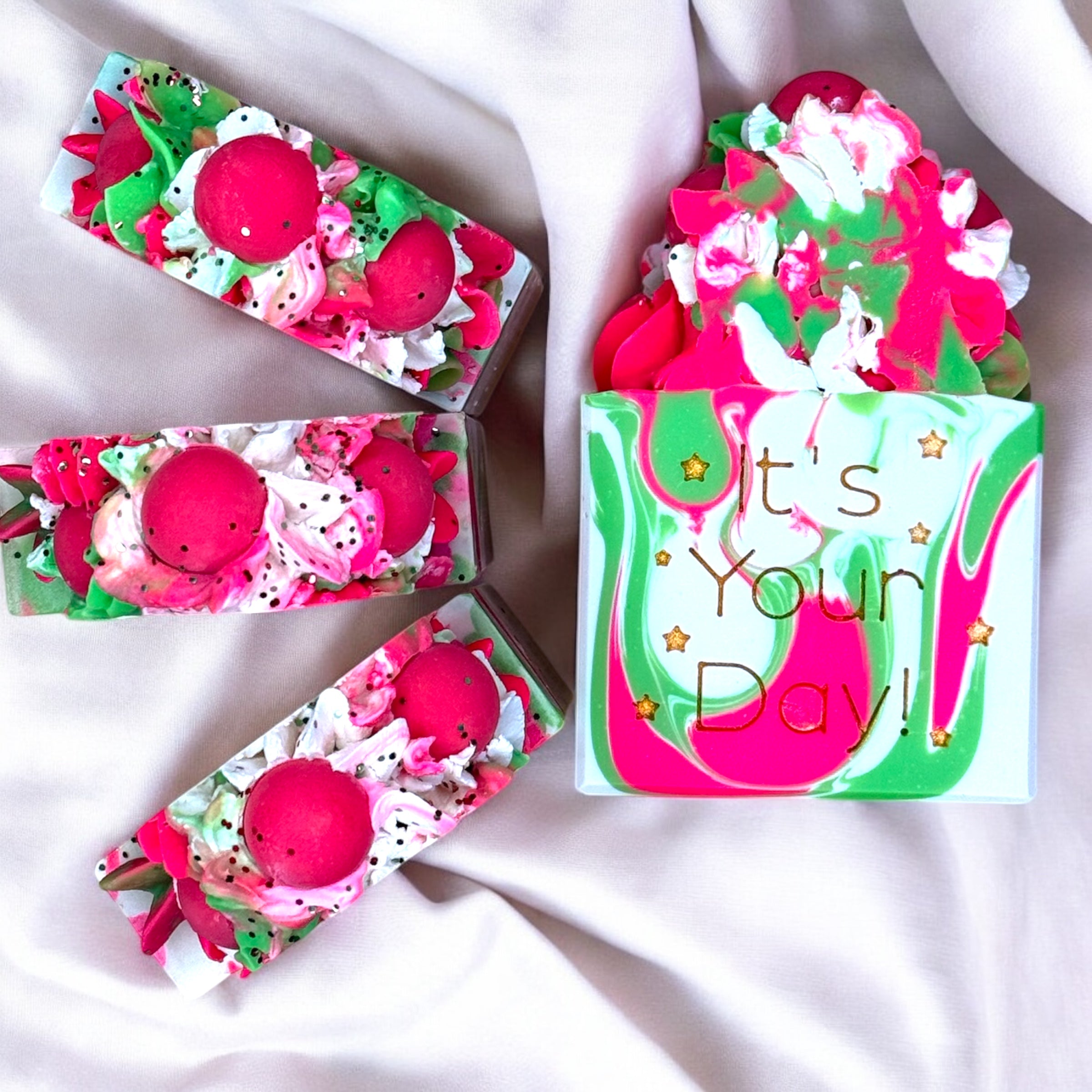 A bar of strawberry kiwi scented soap with a colorful design featuring predominantly pink and green hues, and text that reads 'It's Your Day!'.