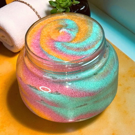 Colorful sugar scrub in a clear plastic jar on a wooden surface. 