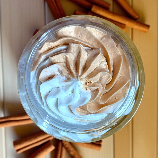 Top view of a container with whipped soap and cinnamon sticks on a wooden surface